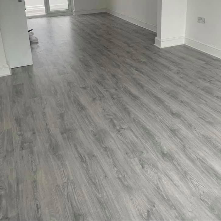 Completed grey wood-look vinyl plank floor in an empty room with white baseboards
